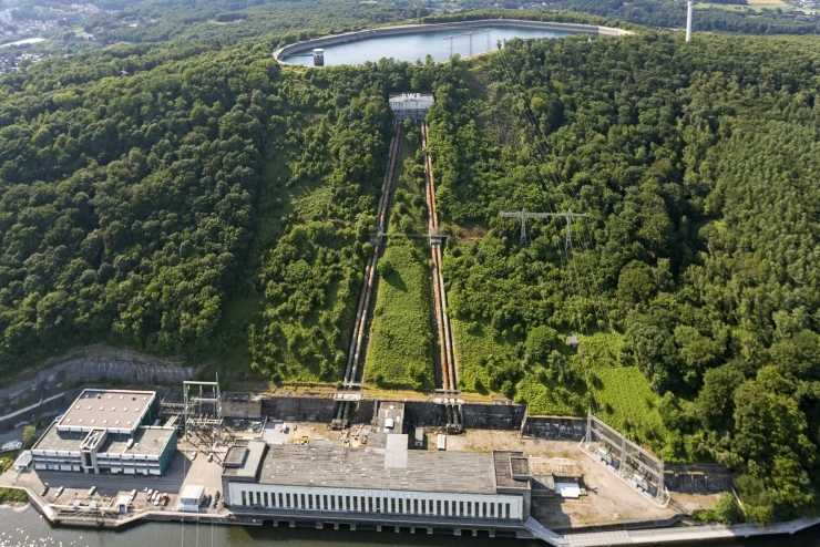 Luftaufnahme: Parallel verlaufende Pipelines verbinden ein Wasserkraftwerk mit einem hoch gelegenen Wasserbecken.