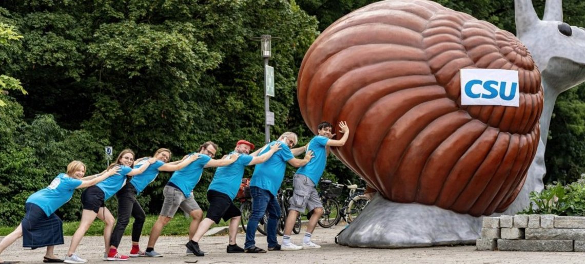 Menschen stehen an der riesigen Statue einer Schnecke und schieben sie an