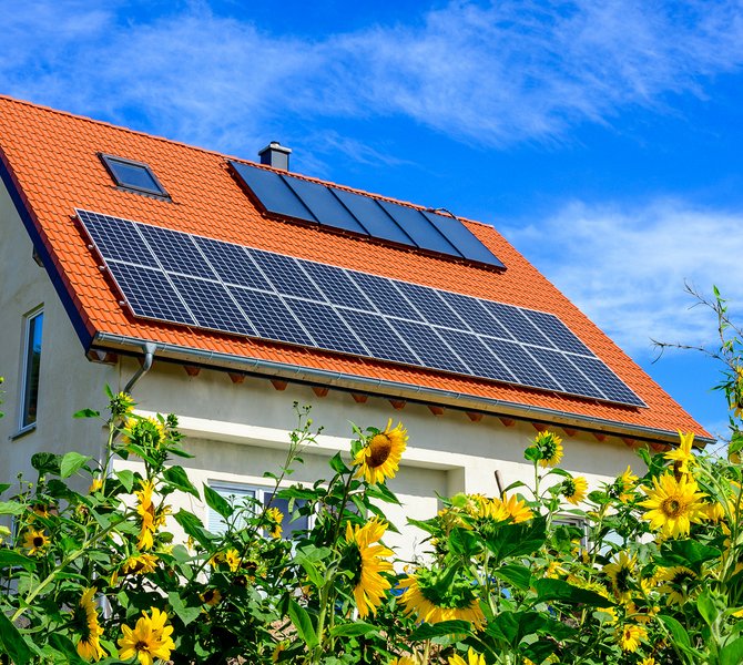 Haus mit Solartechnik auf dem Dach und Sonnenblumen herum