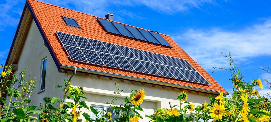 Haus mit Solartechnik auf dem Dach und Sonnenblumen herum