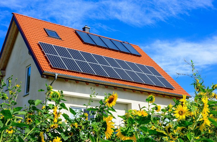 Haus mit Solartechnik auf dem Dach und Sonnenblumen herum