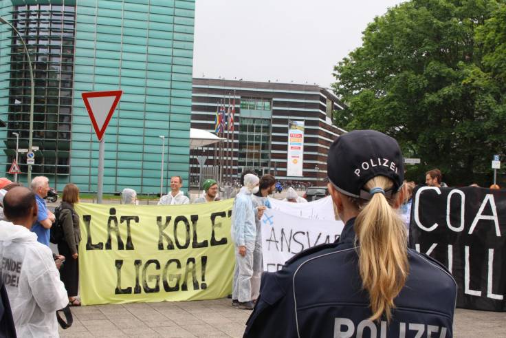 Eine Polizistin beobachtet Aktivisten, deren Banner mit schwedischen Anti-Kohle-Slogans beschriftet sind.