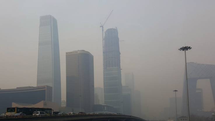 Im graugelben Smog sind gigantische, teils futuristisch anmutende Wolkenkratzer zu erkennen; einige davon sind noch im Bau.