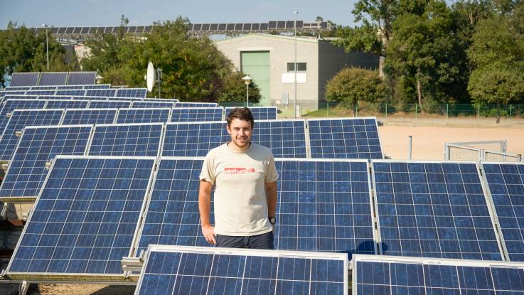 A man in a T-shirt in the countryside surrounded by solar modules.