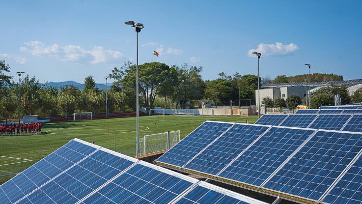Soccer pitch, in the foreground photovoltaic systems, in the background the pitch with floodlight masts.