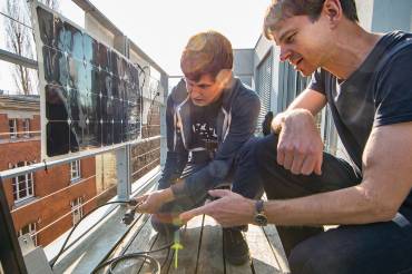 Zwei junge Männer bei der Montage eines Solarmoduls auf einem Balkon