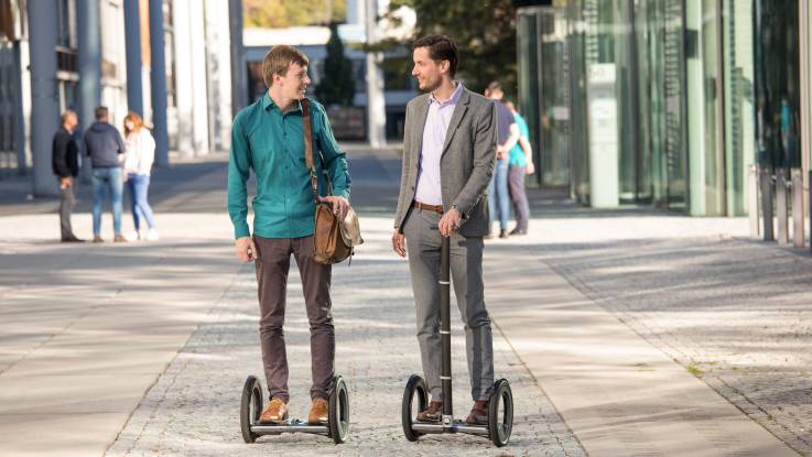 Zwei Unternehmensgründer auf E-Floatern in einer Fußgängerzone