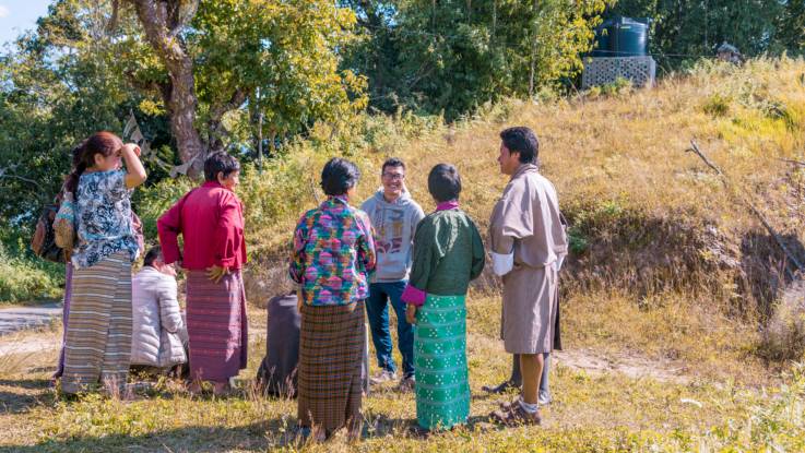 Am Rande eines Weges stehen und sitzen acht Bhutanesen und plaudern entspannt.