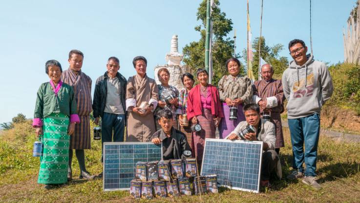 Gruppenfoto: Menschen mit traditioneller Kleidung hinter zwei Solarmodulen.