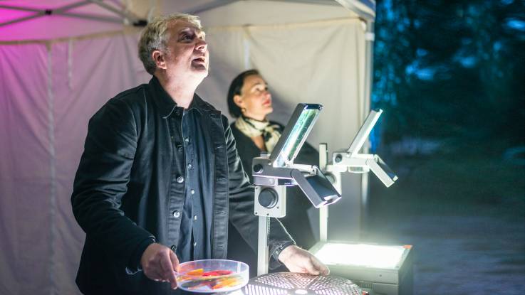 Ein Mann vor einem Partyzelt erzeugen mit zwei Overhead-Projektoren Lichteffekte.