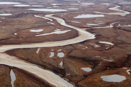 Luftbild einer rostbraunen, kargen Landschaft mit vielen kleinen Wasserflächen und einem Fluss.