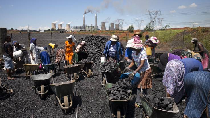 Vor einem Kohlekraftwerk füllen Menschen Kohle in ihre Schubkarren.