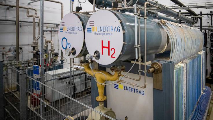 Zwei runde, liegende Tanks in einer Industriehalle, beide mit dem Unternehmensnamen «ENERTRAG» beschriftet, auf dem einen der Tanks steht in großen blauen Lettern zudem «O₂», auf dem anderen «H₂» in Rot
