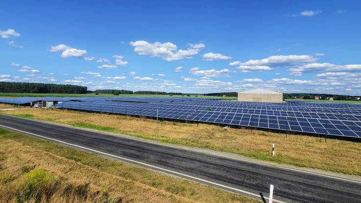 A solar farm of PV modules runs alongside a country road.