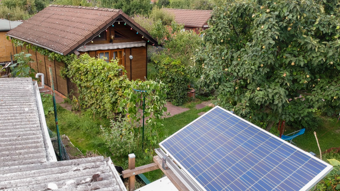 Luftaufnahme einer Fotovoltaik-Panele, die oberhalb eines Kleingartenhauses im Grünen aufgebaut ist.