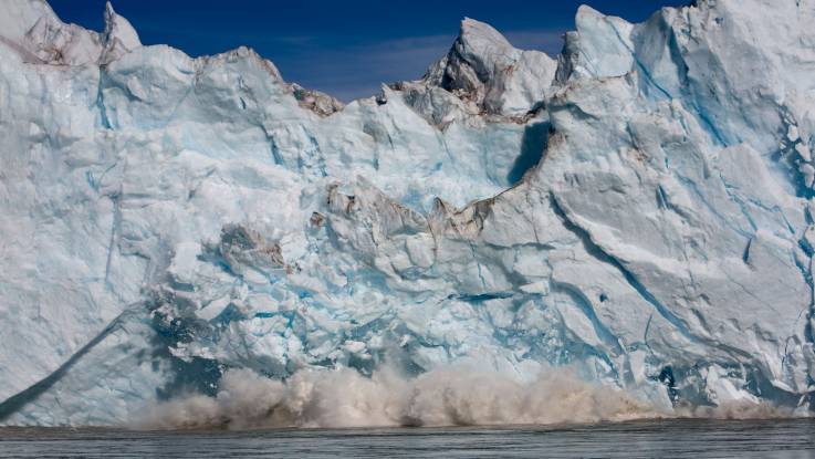 Von einer Gletscherfront bersten riesige Teile und fallen ins Wasser.