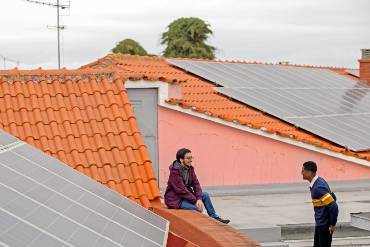 In the midst of a rooftop landscape with PV systems, two young men stand talking happily.
