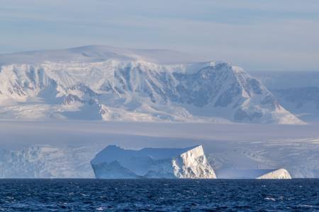Eisberge im tiefblauen Wasser, dahinter schneebedeckte Berge