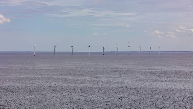 Off the coast, ten wind turbines stand on small piers in the sea - the water looks gray and rugged.