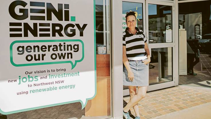 Eine Frau mit Zopf steht in Rock und mit schwarz-weiß gestreiftem Oberteil neben einem Plakat der "Geni Energie".