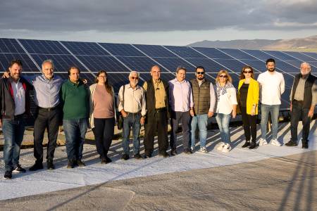 Eine dreizehnköpfige Gruppe steht aufgereiht vor einer langgestreckten Photovoltaikanlage.