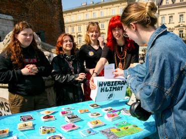 Junge Frauen stehen an einem Stand voller Flyer: eine von ihnen wirft einen Zettel in eine Box mit der Aufschrift «Wybierz klimat». 