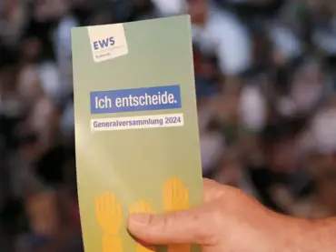 Jemand hält eine Karte mit der Aufschrift «EWS – Ich entscheide – Generalversammlung 2024» ins Bild