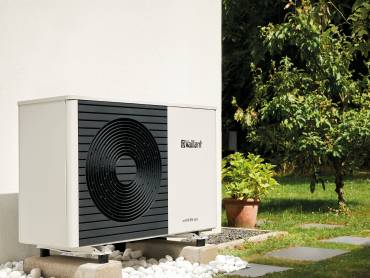 Am Balkon eines mit reichlich Pflanzen geschmückten Balkons ist eine Balkon-PV-Anlage montiert. Im Hintergrund eine Backsteinmauer.