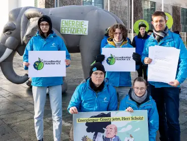 Fünf Menschen in blauen Jacken präsentieren im Freien das Logo des Umweltinstituts; hinter ihnen die Skulptur eines Elefanten, darauf steht «Energieeffizienz».