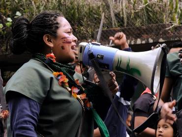 Eine indigene Frau mit Gesichtsbemalung spricht in eine Megafon