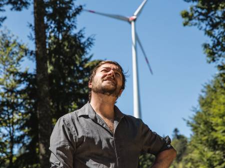 Sebastian Sladek steht, die Hände in die Hüften gestemmt, vor einem Windkraftwerk