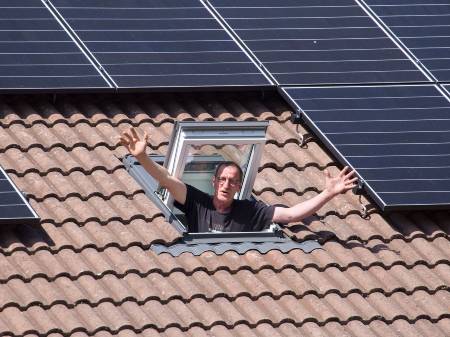Ein Mann winkt aus einem Dachfenster, um ihn sind PV-Module installiert