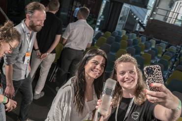 Susan Miklaw und Michelle Pfitzer von eco:fibr machen ein Selfie mit ihrer Trophäe, im Hintergrund weitere Personen