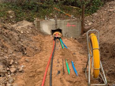 In einem Graben liegen verschiedene Rohrleitungen, die aus einer betonierten Unterführung unter einem Bahndamm entspringen