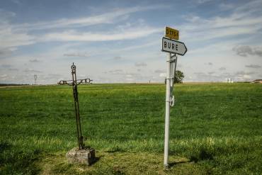 Ein Wegkreuz neben einem Schild, das zur französischen Gemeinde Bure weist.