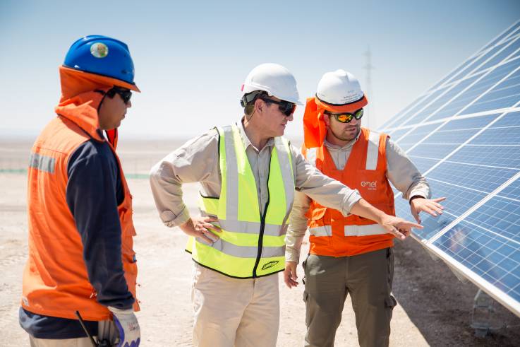 Drei Männer eines Wartungsteams begutachten die PV-Module; sie tragen Helme mit Nackenschutz, um sich vor der Sonne zu schützen.