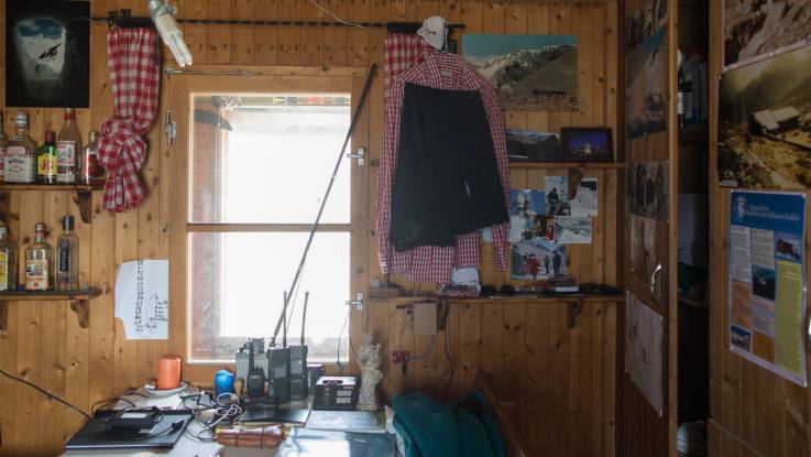 Die holzverkleideten Innenwände der Station schmücken historische Fotografien; auf einem Tisch stehen Funkgeräte, auf dem Wandregal einige Schnapsflaschen.