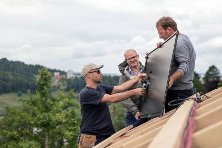 Ein Mann hält ein Solar-Modul, zwei andere inspizieren es vor dem Platzieren.