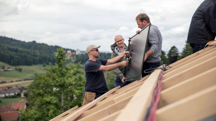 Roger Spycher hält ein Solar-Modul, zwei andere inspizieren es vor dem Platzieren.