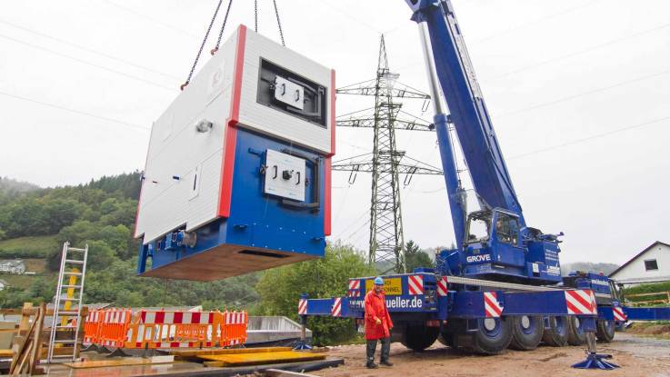 Ein Kranwagen senkt einen containergroßen Brennkessel ab.