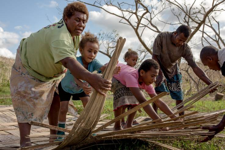 Eine Familie flechtet mit ihren Kindern aus Leisten einen neuen Fußboden für ein Haus. 