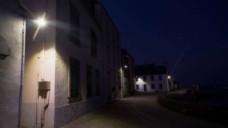 Straße im Dorf bei Nacht, an einer Hausecke brennt eine Straßenlampe.