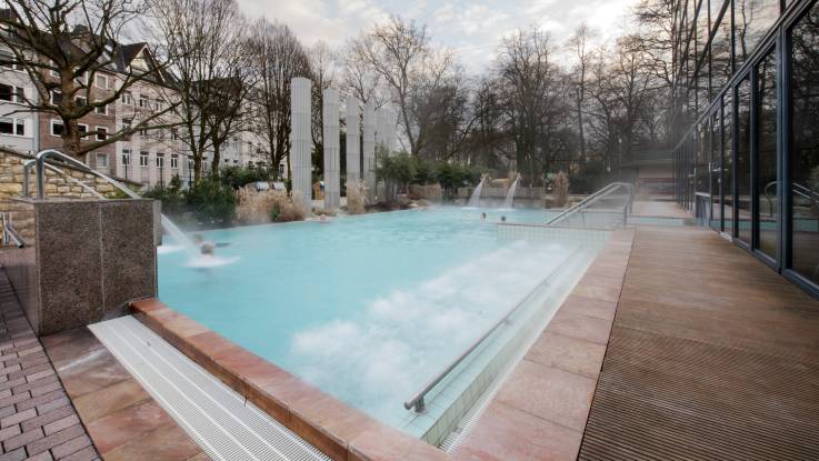 Außenschwimmbecken im Winter, aus vier Wasserhähnen ergießt sich das dampfende Thermalwasser in das Becken