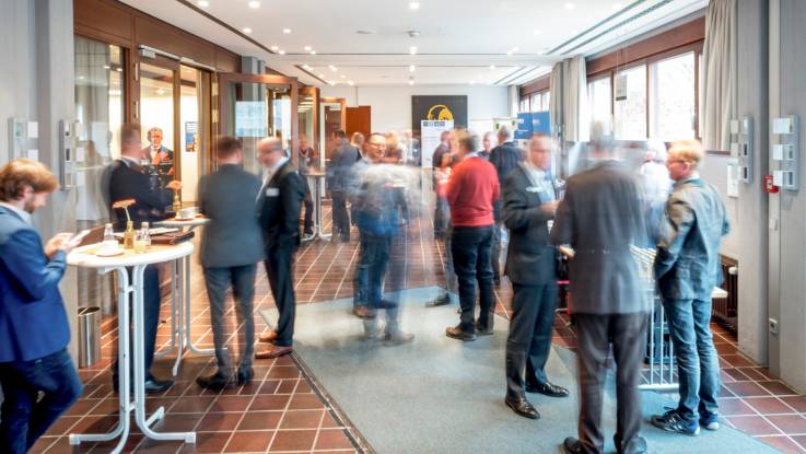 Im Foyer der Biberacher Stadthalle Menschen an Stehtischen, in Bewegungsunschärfe fotografiert.