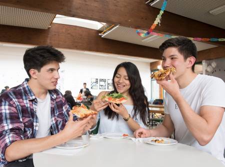 Drei ältere Schüler essen Pizza aus der Hand.