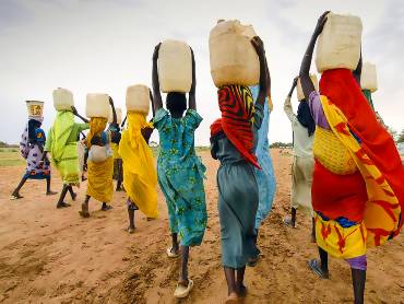 Eine Gruppe Frauen, Kanister auf dem Kopf, ist auf dem Heimweg von einer Wasserstelle.