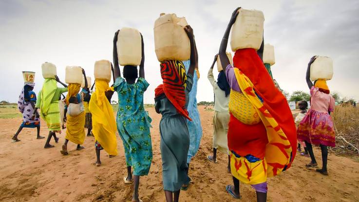 Eine Gruppe Frauen, Kanister auf dem Kopf, ist auf dem Heimweg von einer Wasserstelle.