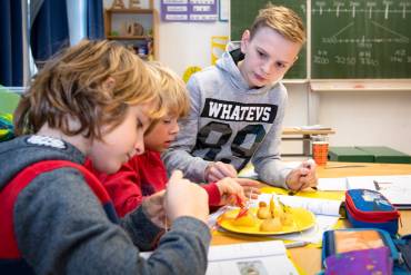 Ein älterer Junge schaut zwei jüngeren Schülern beim Basteln zu.