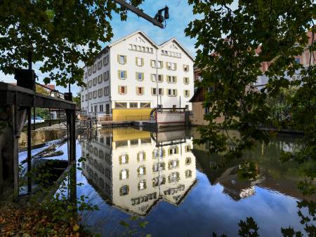 Ein großes Haus mit zwei Satteldächern spiegelt sich im Wasser.