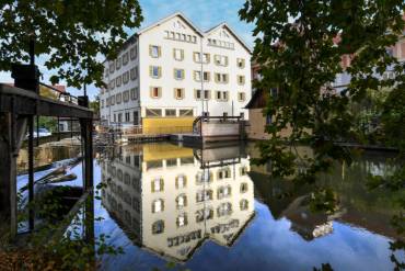 Ein großes Haus mit zwei Satteldächern spiegelt sich im Wasser.